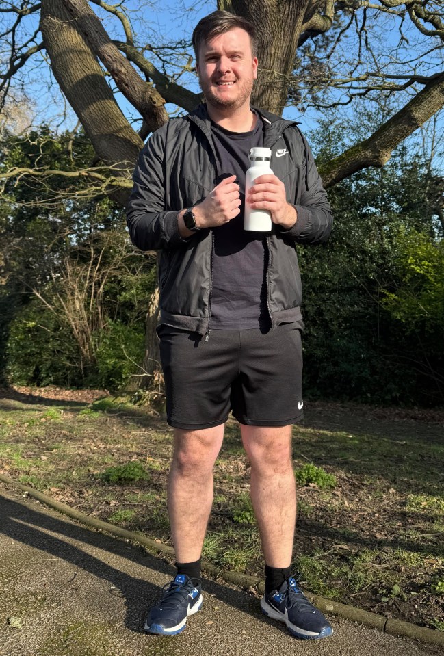 Man in athletic wear holding a water bottle in a park.