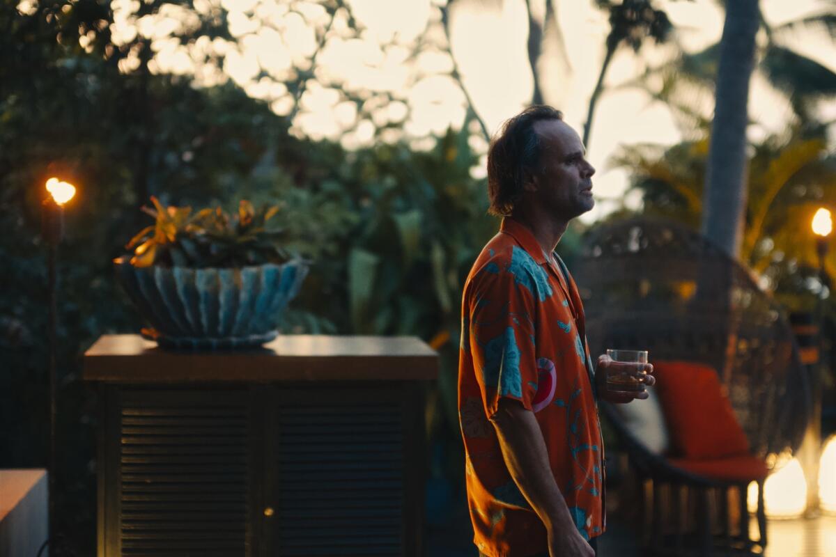 A profile view of a man in a red and blue Hawaiian shirt standing outdoors holding a glass