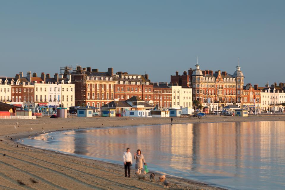 Dog walkers on Weymouth beach at dawn.