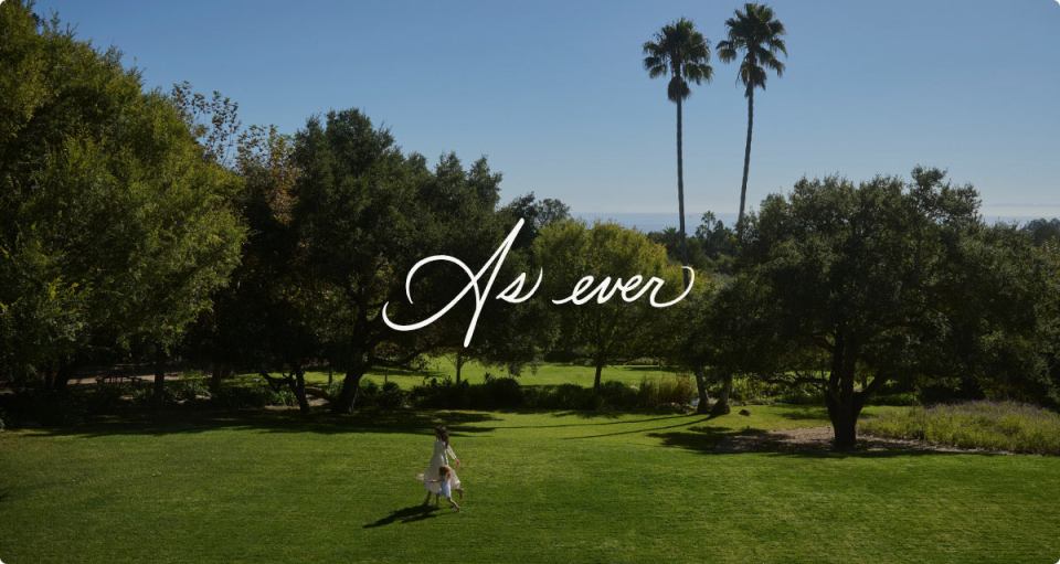 A woman and child walking on a grassy lawn, with palm trees and text overlay reading "As ever".