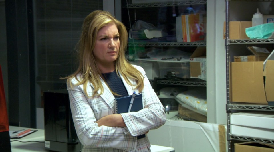 Karren Brady with arms crossed, holding a notebook.