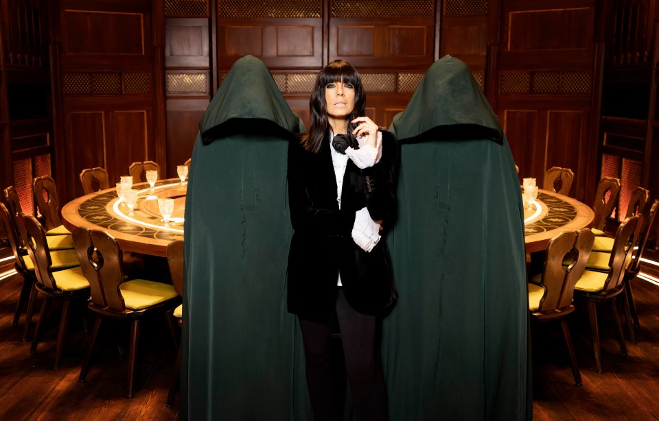 Claudia Winkleman on the set of The Traitors, flanked by figures in dark robes.