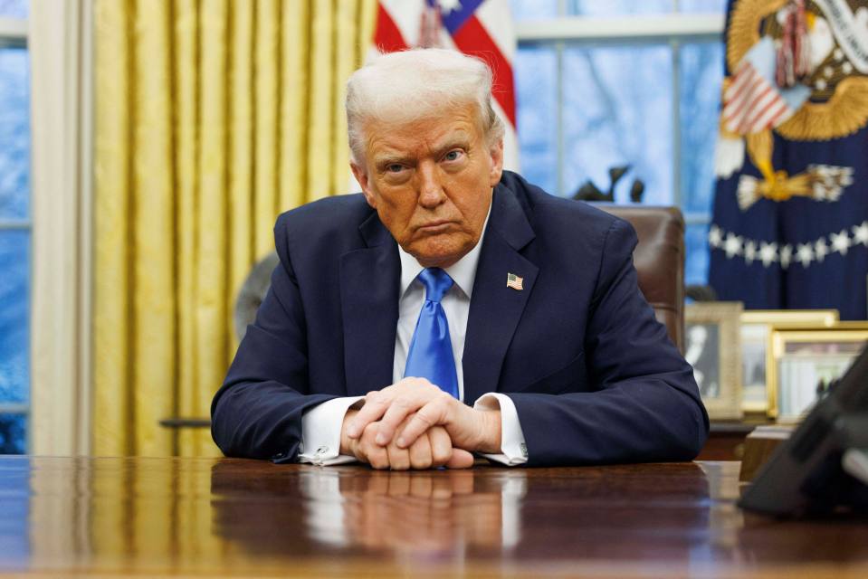 President Donald Trump seated at the Resolute Desk in the Oval Office.