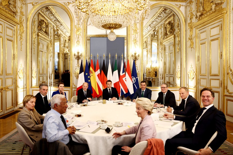 Politicians at a round table meeting in a grand room.