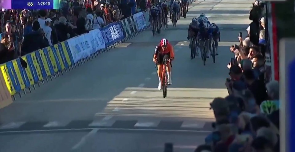 Cyclist in orange jersey leading a race, spectators watching.