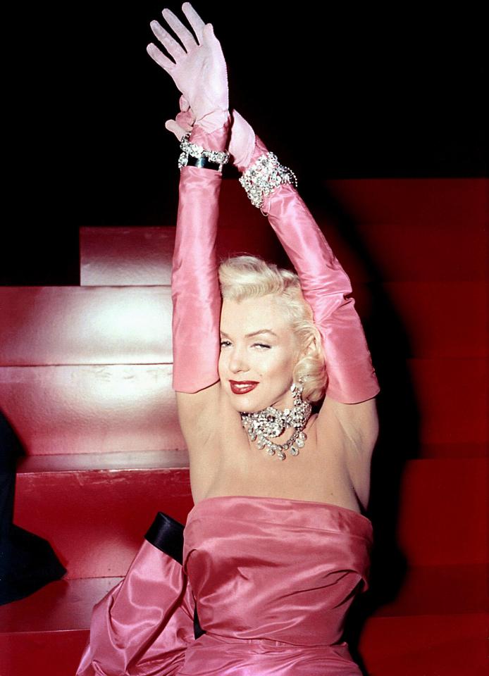 Marilyn Monroe in a pink gown and long gloves, wearing diamond jewelry.