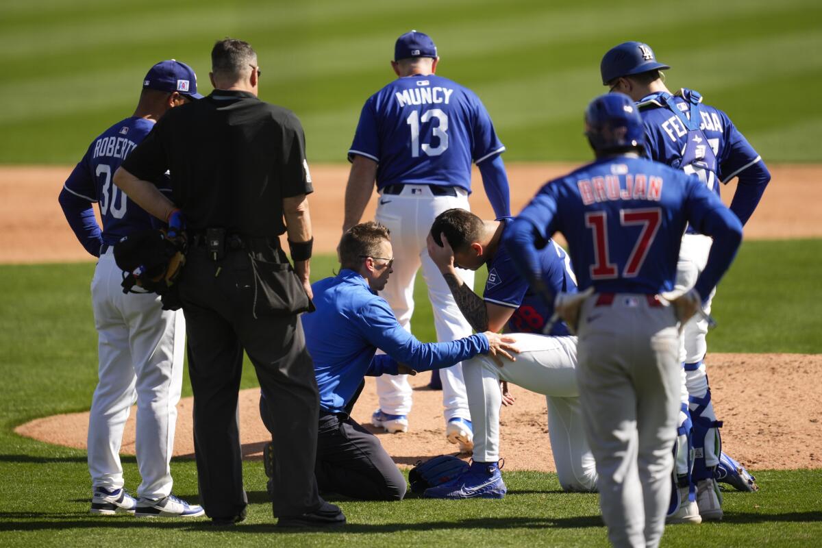 Dodgers pitcher Bobby Miller speaks with a team trainer after taking a comebacker off his head.