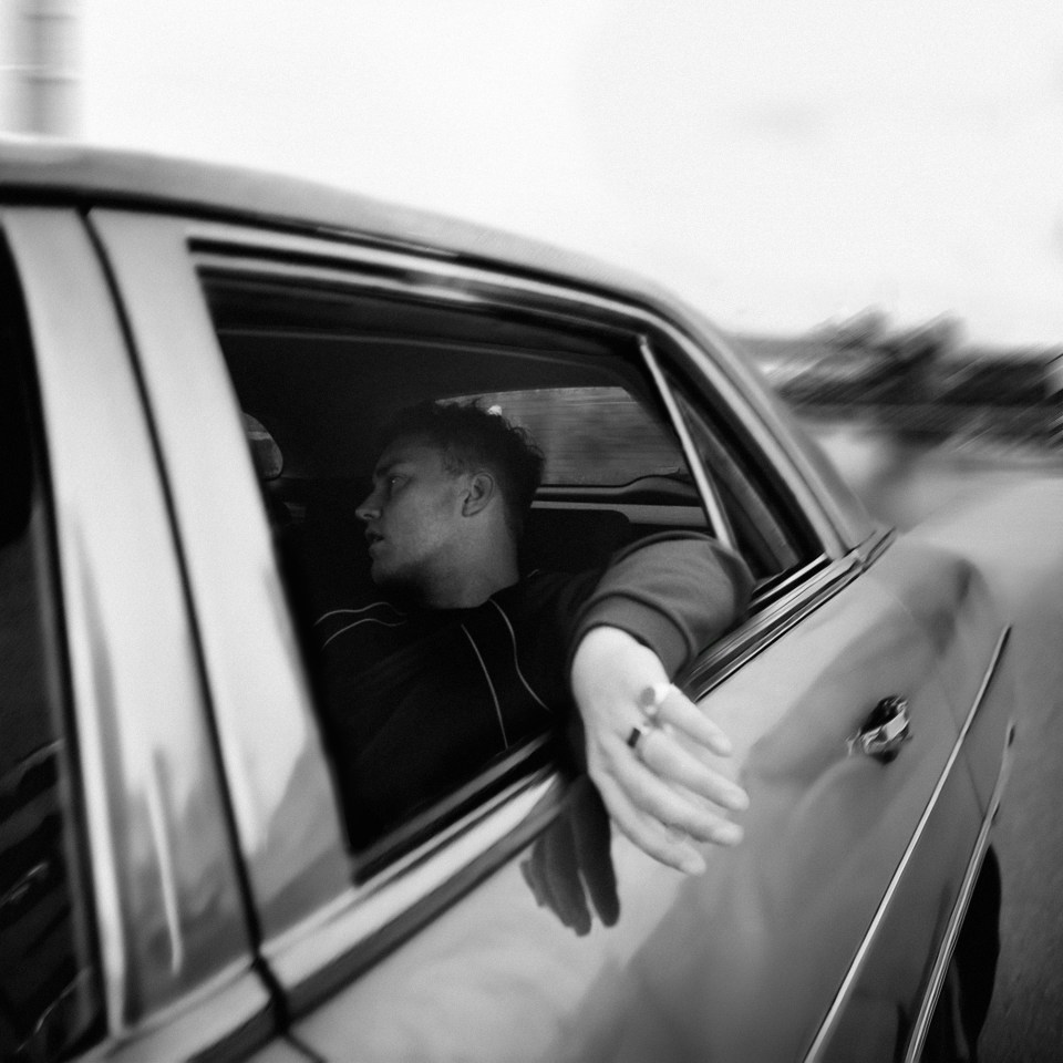 Black and white photo of Sam Fender leaning out of a car window.