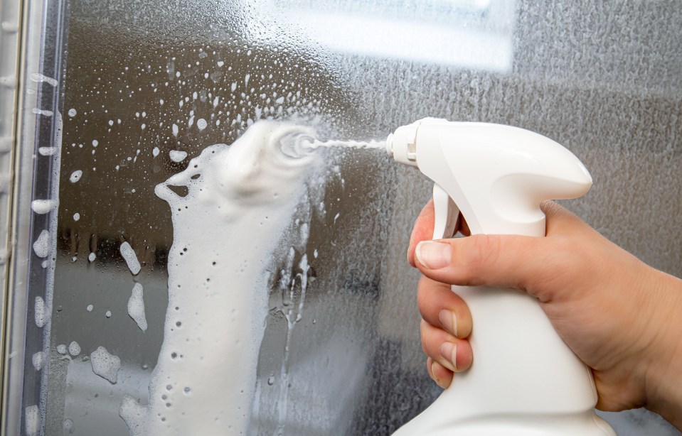 Person hand using limescale remover chemical foam. Descaling shower case glass door. Work in progress.