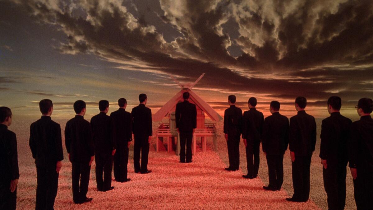 People in black suits stand in front of a dramatic, strange skyline.