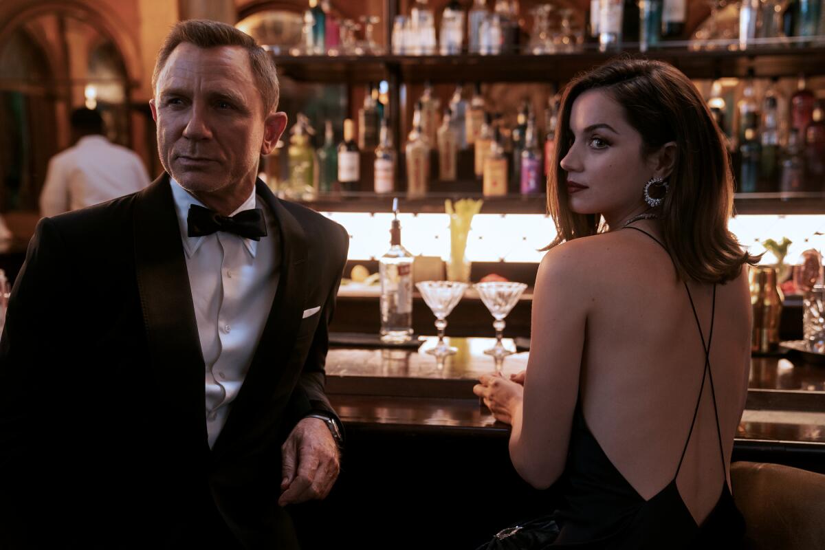 A man in a tuxedo and a woman in a dress stand at a bar