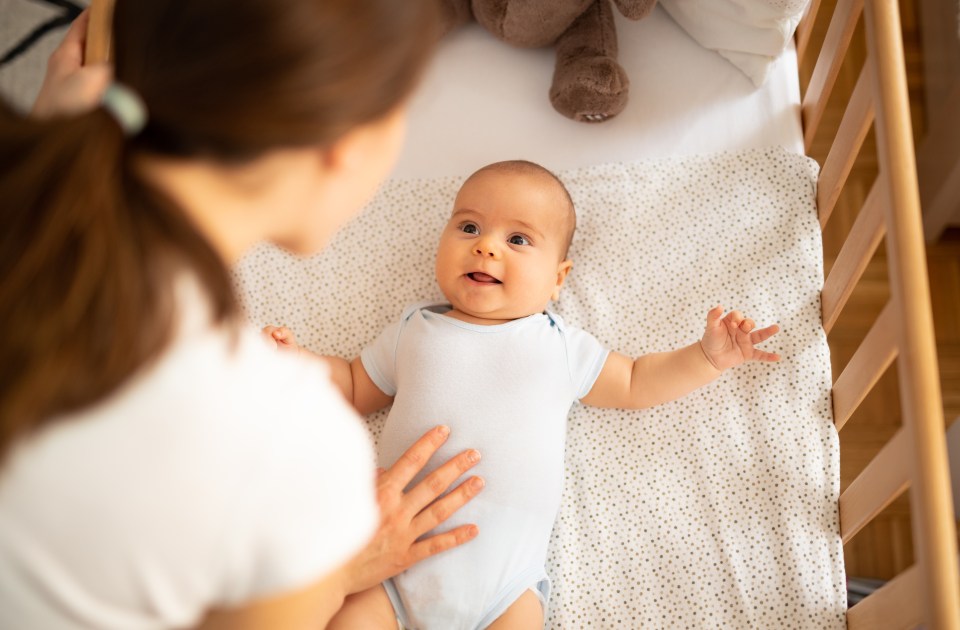 Mother leaning over crib, talking to her smiling baby boy.