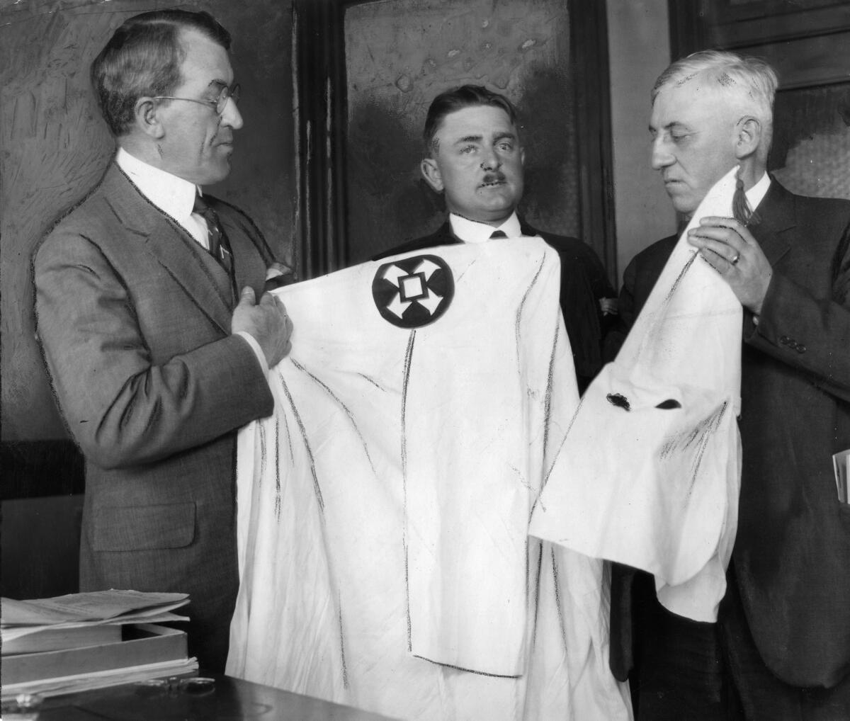 People examine a Ku Klux Klan gown and mask, with peaked cap.