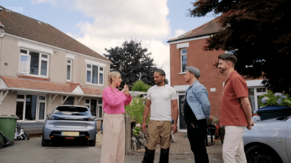 Four people standing outside two houses, talking.