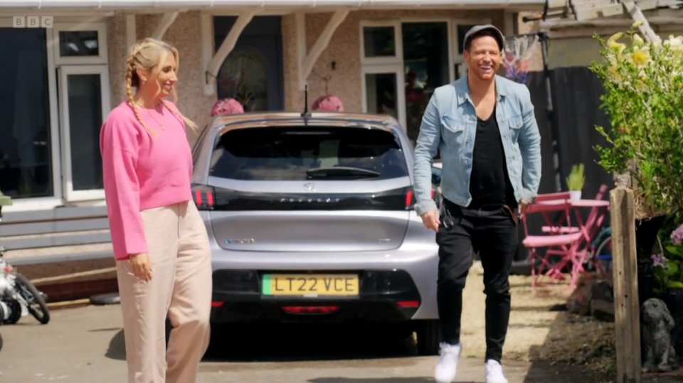 A man and woman walking towards a silver car in front of a house.