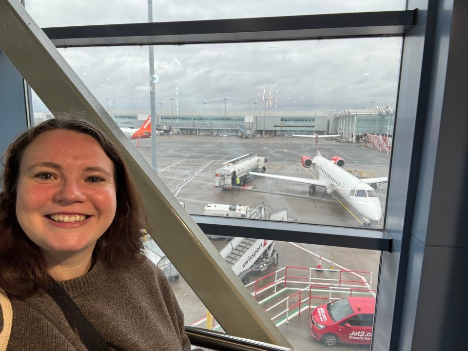 Woman at airport looking out window at airplane.