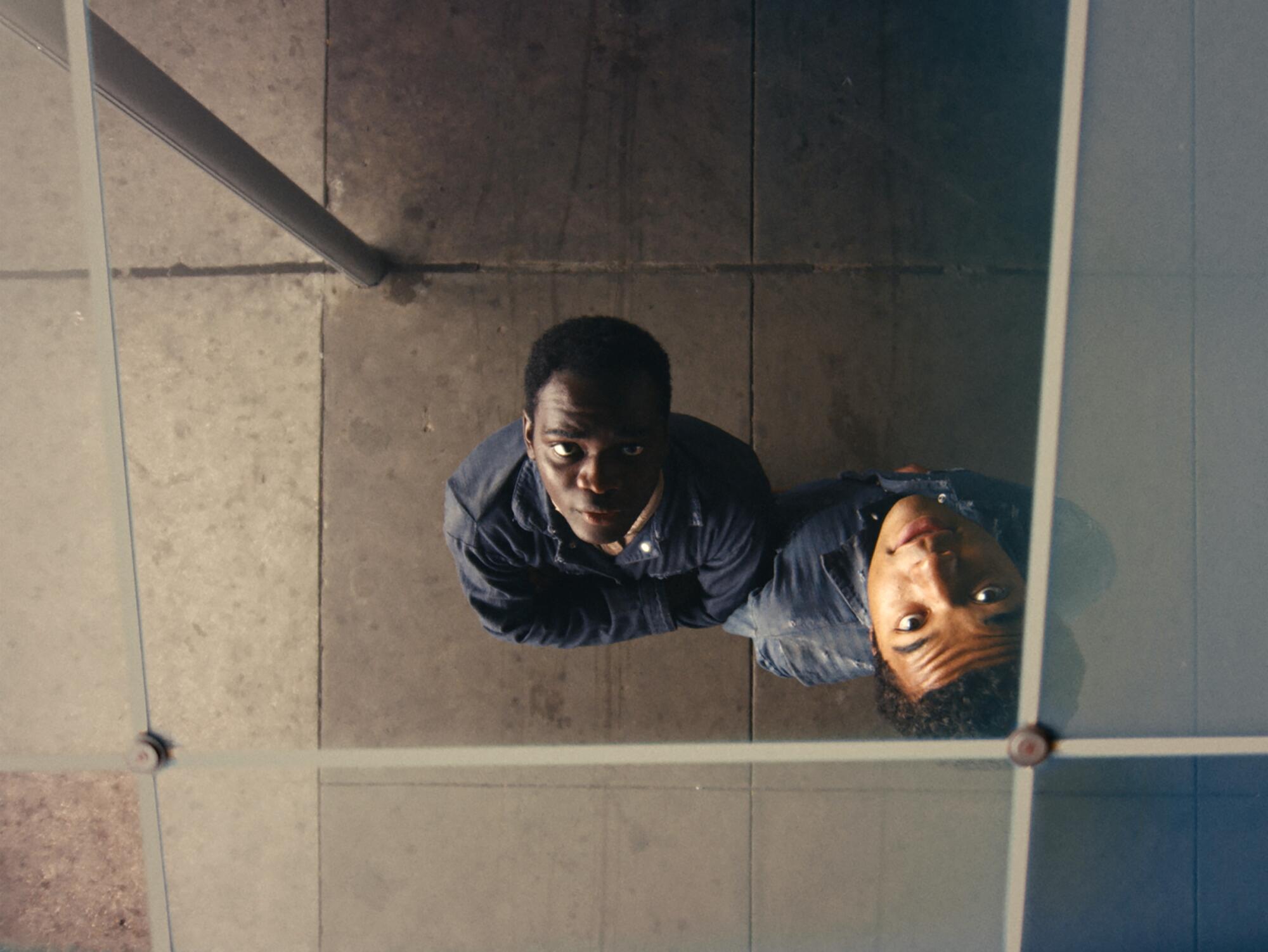 Two young men stare upward at a mirrored ceiling.