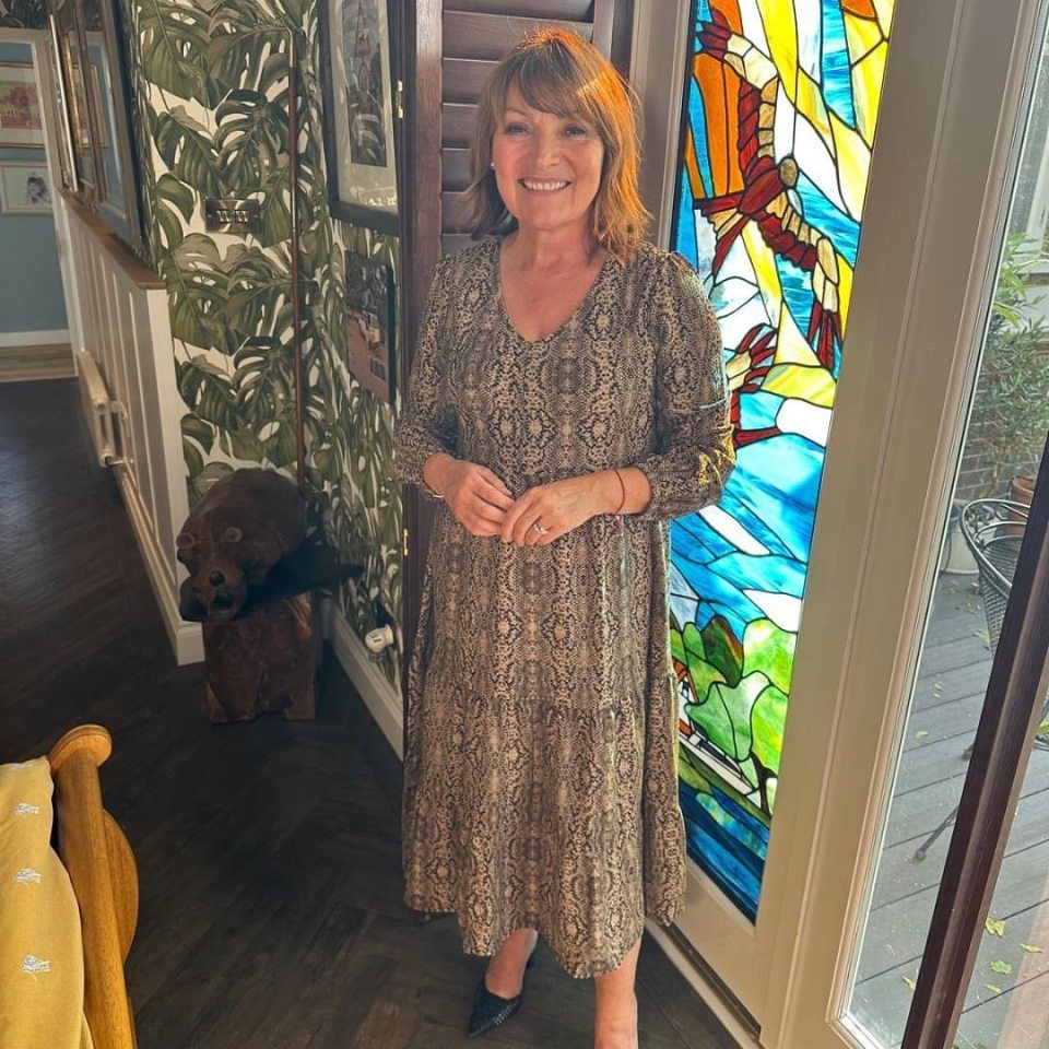 Lorraine Kelly in a snakeskin-print dress, standing by a stained-glass window.