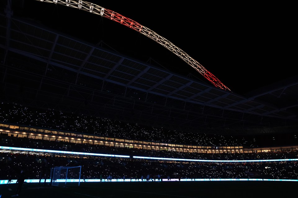 Wembley Stadium at night during a power outage; spectators hold up illuminated phones.