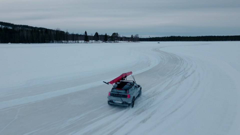 A grey Volvo driving on a frozen lake with a red kayak on its roof rack.