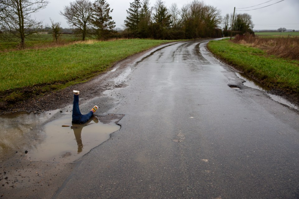 Fake legs in a large pothole on a wet road.