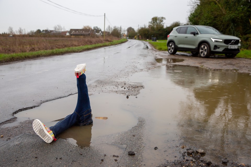 A pair of legs sticking out of a large pothole in a road.