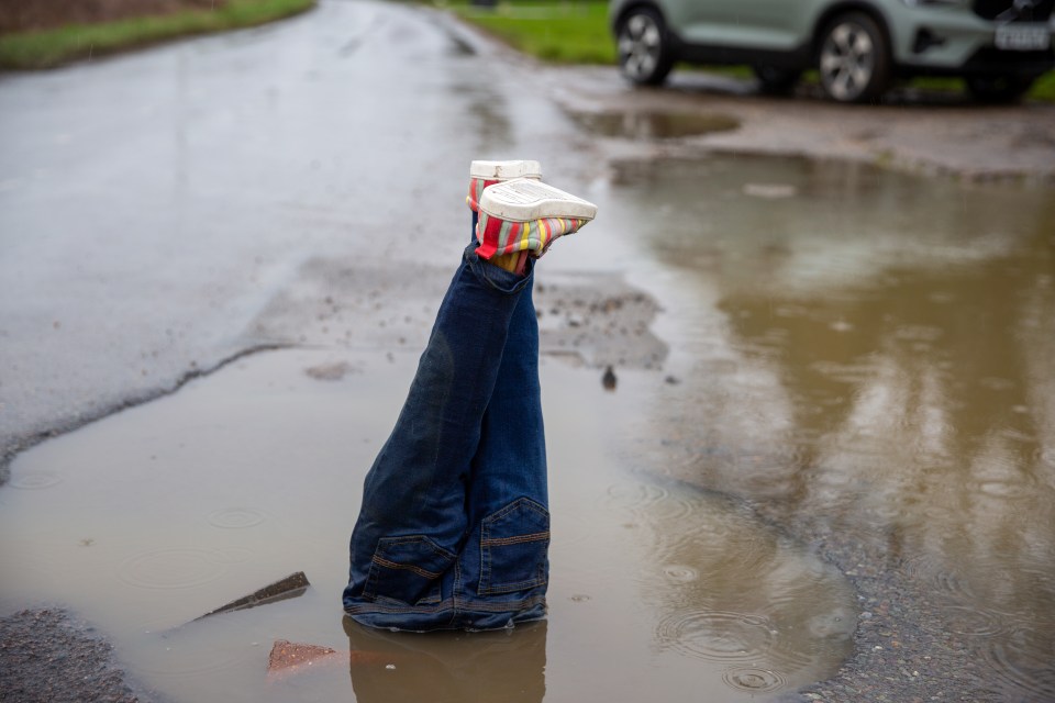 Legs in colorful shoes sticking out of a pothole.