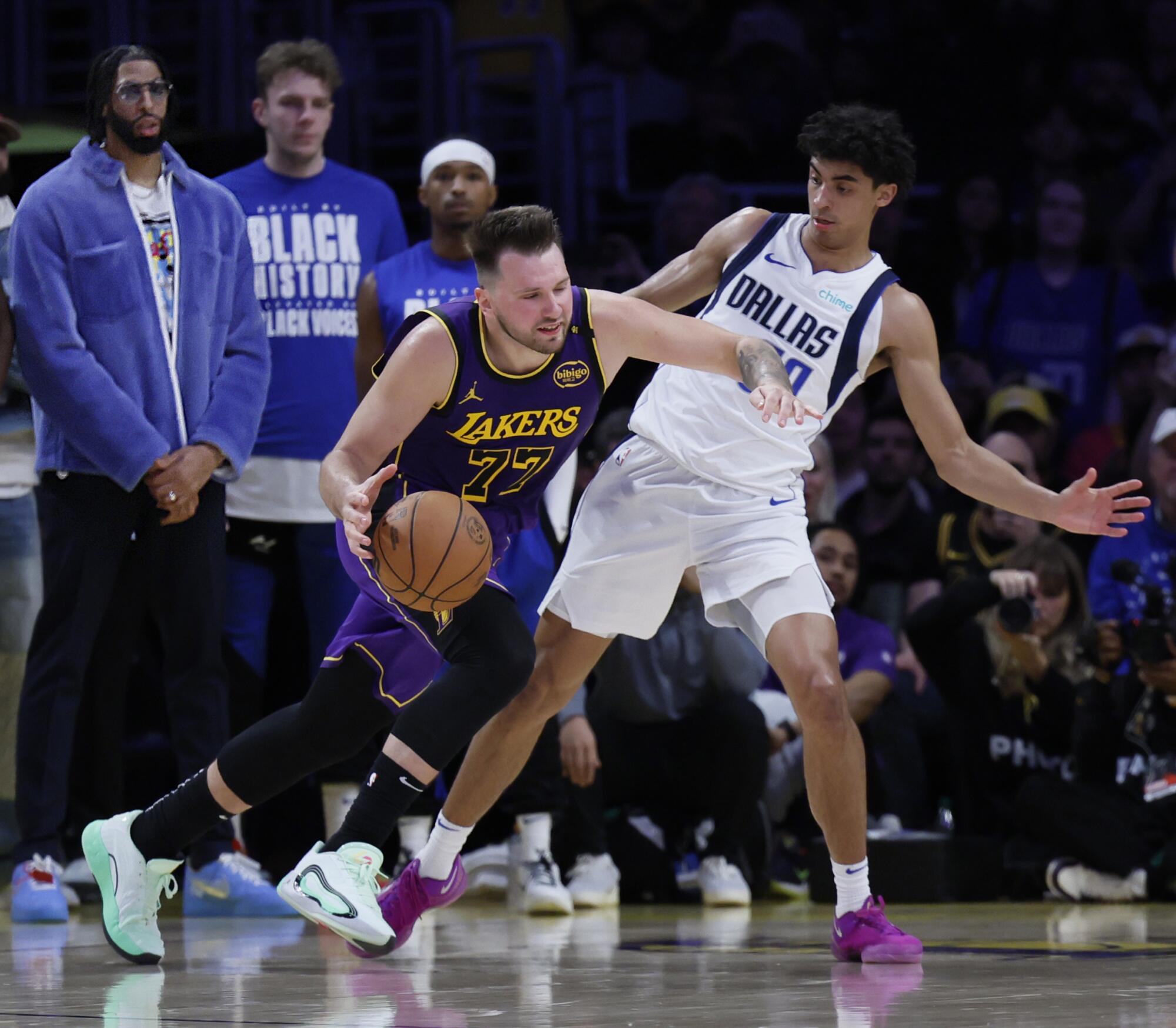 Anthony Davis watches from the sideline as Luka Doncic drives the hoop past Max Christie