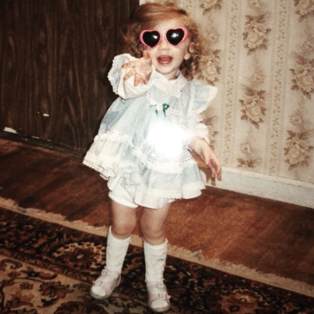 Young girl in a light blue dress and heart-shaped sunglasses.