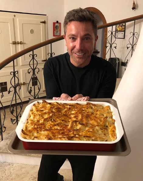 Gino D'Acampo holding a large dish of baked pasta.