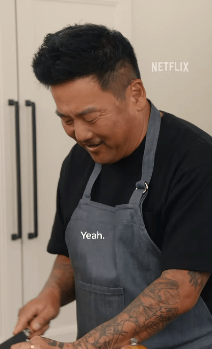 A smiling man wearing a gray apron and a black shirt.