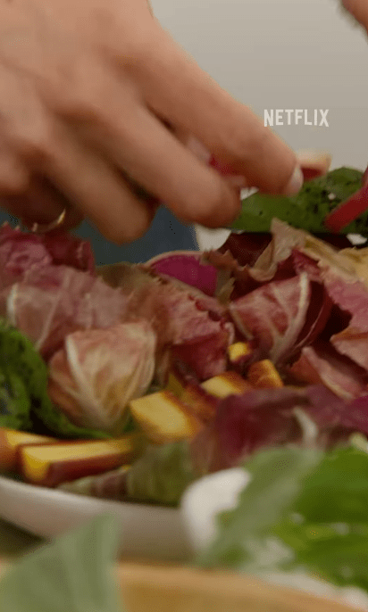 Hands adding greens to a salad.