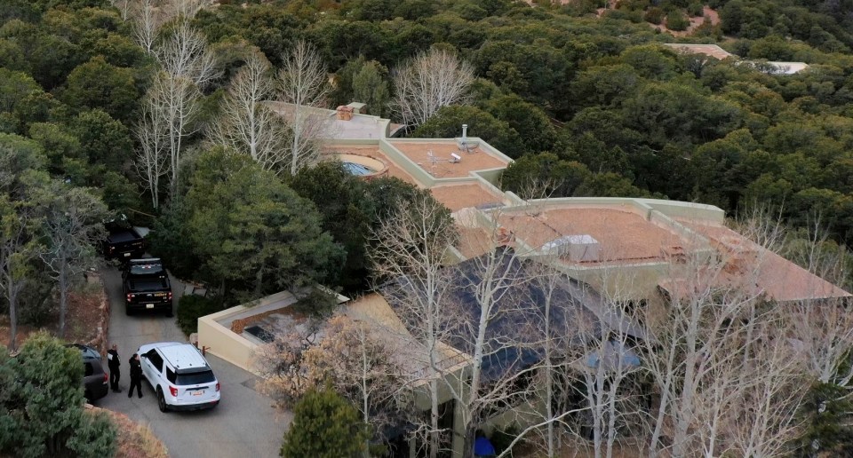 Aerial view of a house surrounded by trees with several police vehicles parked in the driveway.