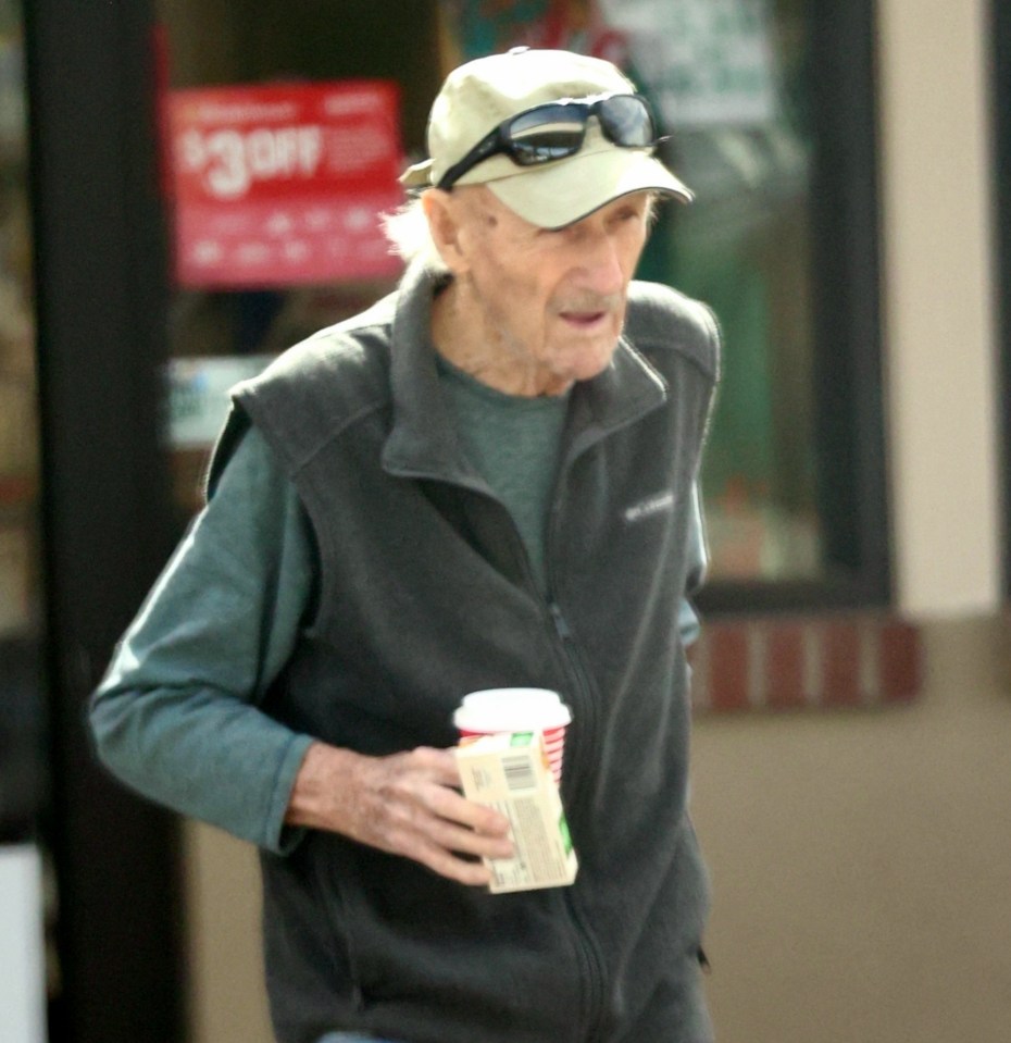 Older man wearing a vest and cap, holding a coffee cup.