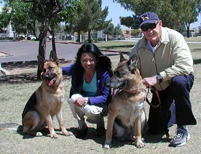 A couple and their two German Shepherds in a park.