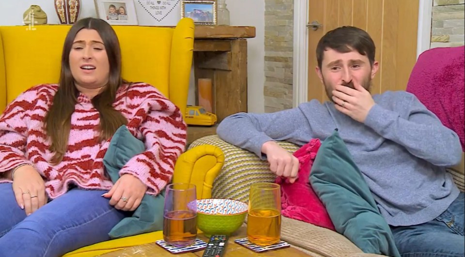 Couple sitting on a yellow couch, man covering his mouth.