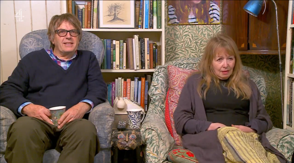 A man and woman sitting in armchairs in a book-filled room.