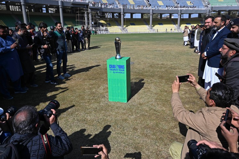 Members of the media and officials gather around the ICC Champions Trophy kept on display during a ceremony at the Arbab Niaz Cricket Stadium in Peshawar on February 6, 2025. The Champions Trophy will feature Pakistan, Australia, England, New Zealand, South Africa, Afghanistan and Bangladesh with the event running from February 19 to March 9, 2025. (Photo by Abdul MAJEED / AFP)