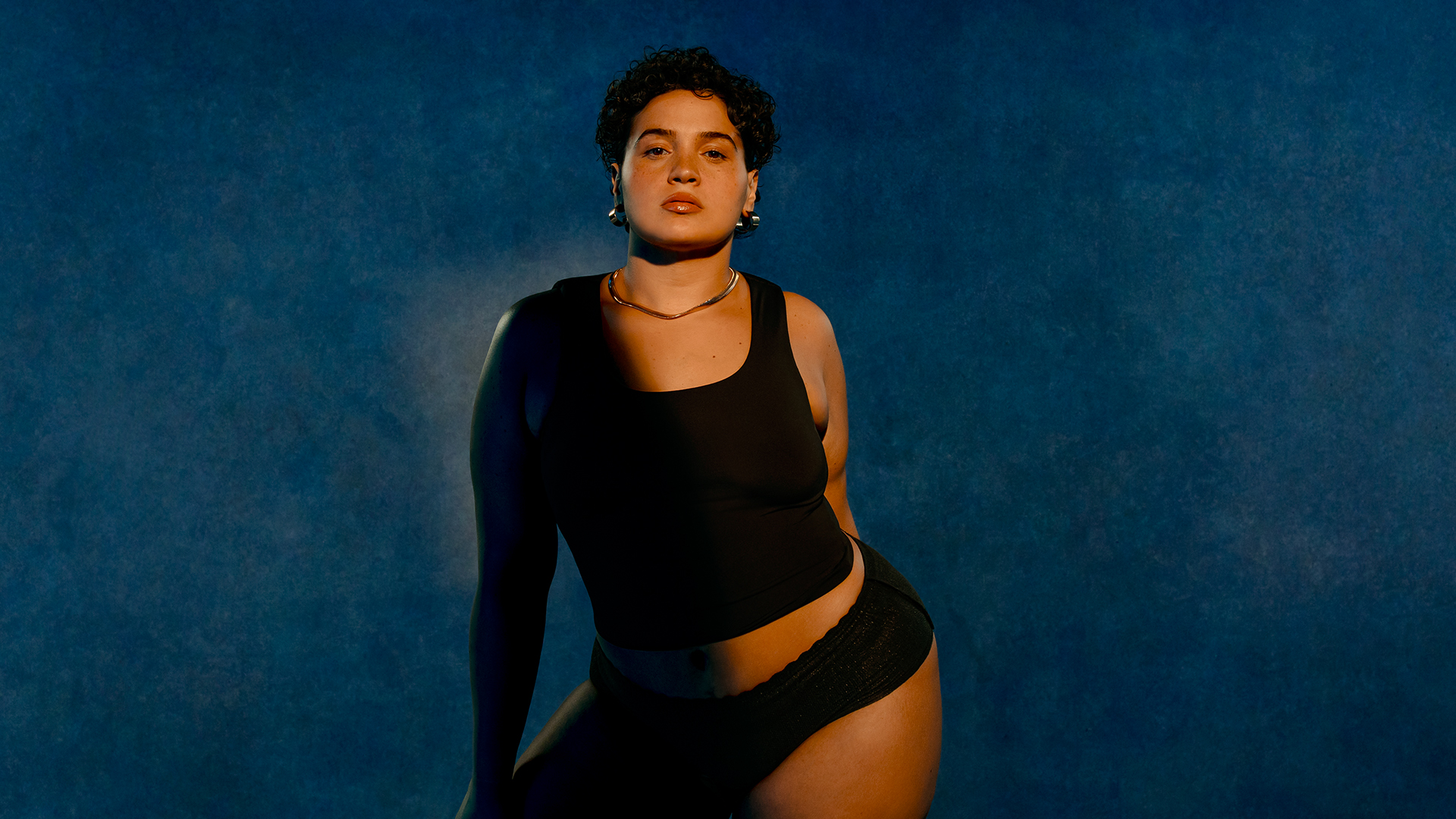 Woman in black top and underwear against a blue background.