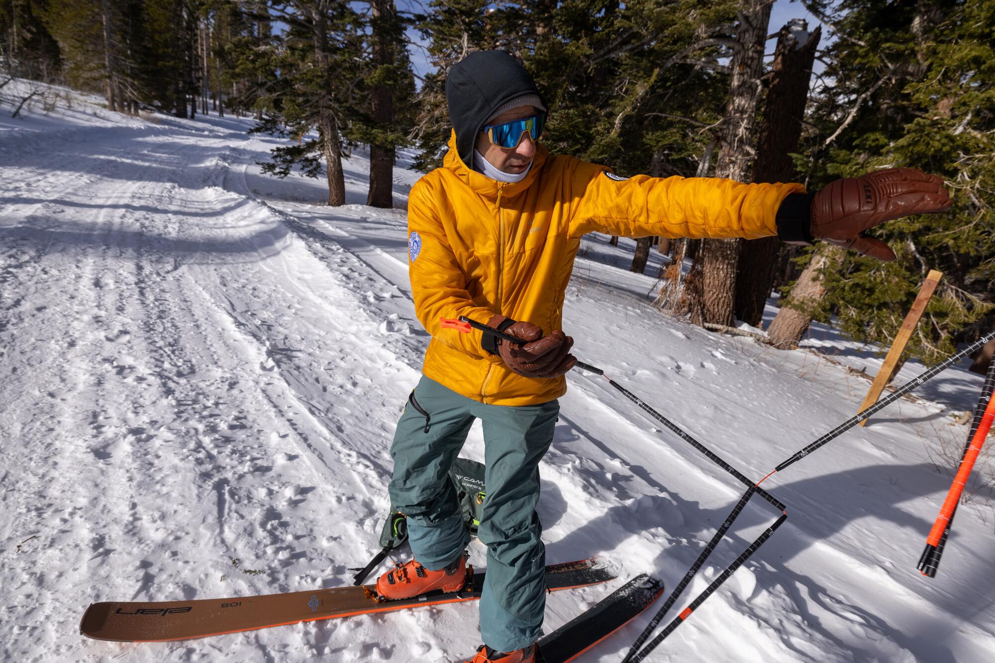 A skier wearing a gold jacket demonstrates the use of avalanche probes.   