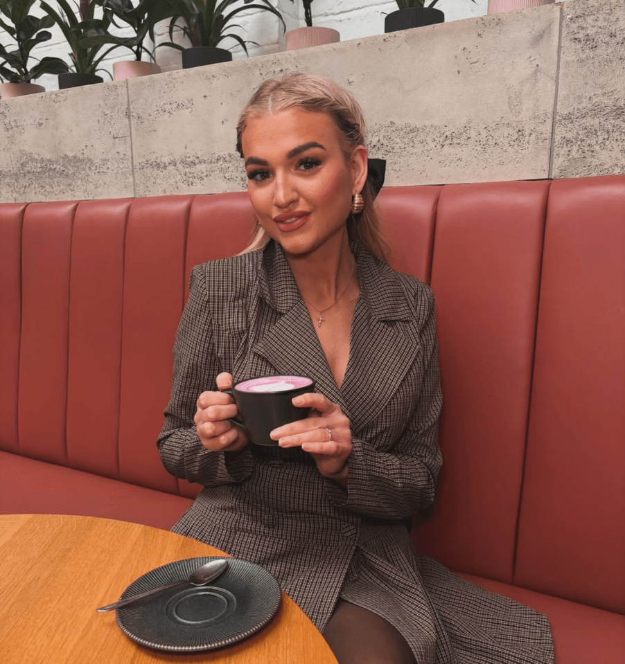 Woman in a brown blazer sitting on a red booth, holding a cup of pink latte.