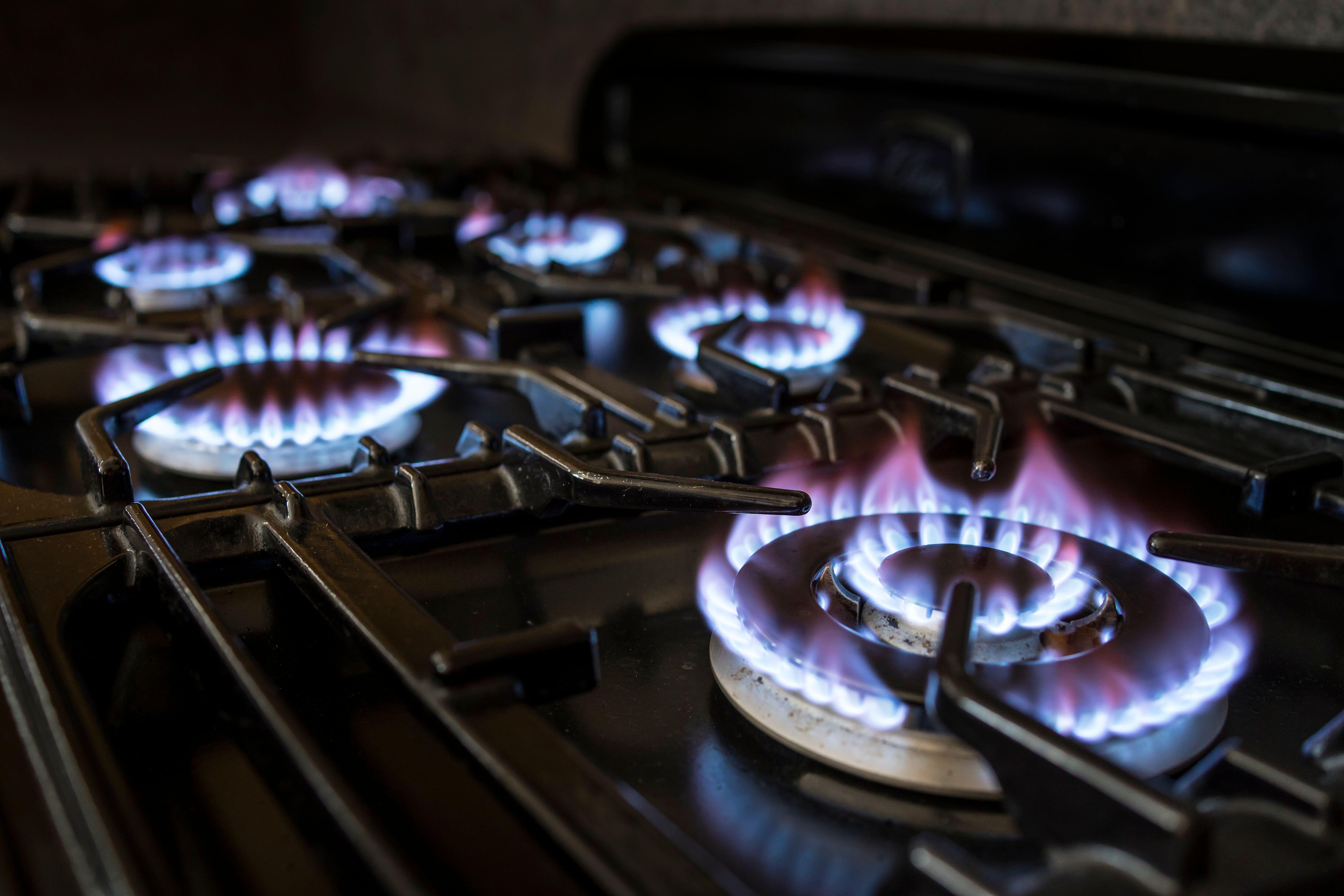 2HMK726 Close up of flaming gas rings lit on the hob of a domestic gas cooker in a UK kitchen setting.