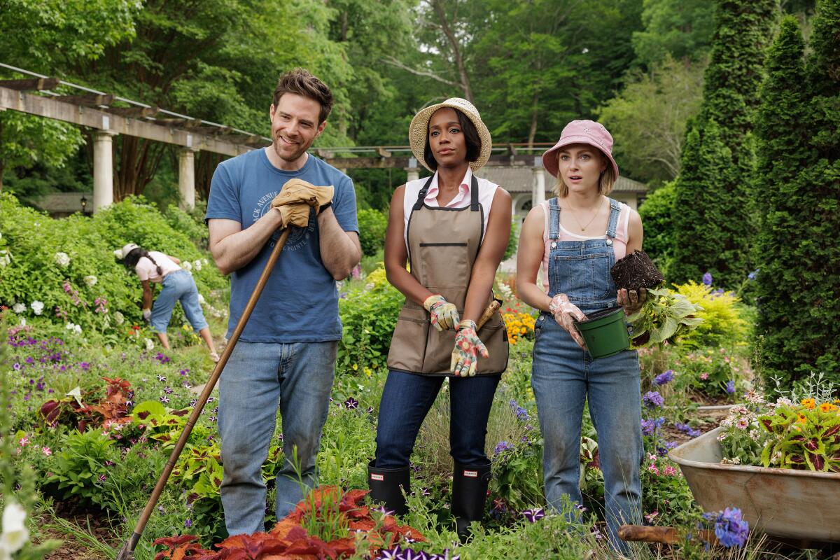 A man holding a hoe standing next to two women in a garden.