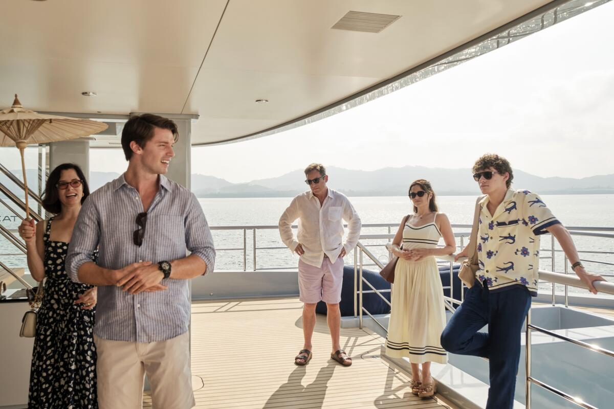 A family stands on the platform of a yacht with the ocean and mountains visible on the horizon.