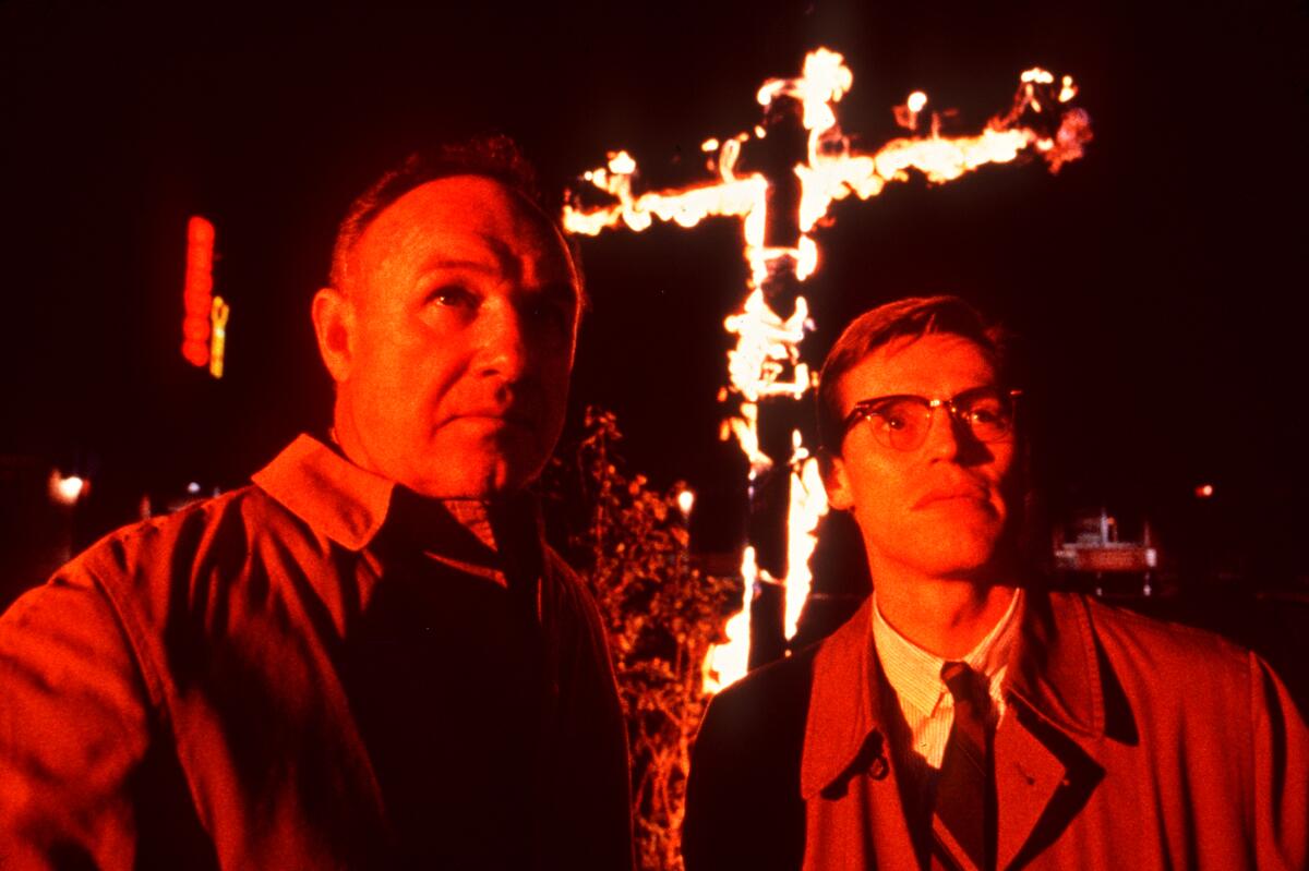 Two men stand in front of a burning cross.