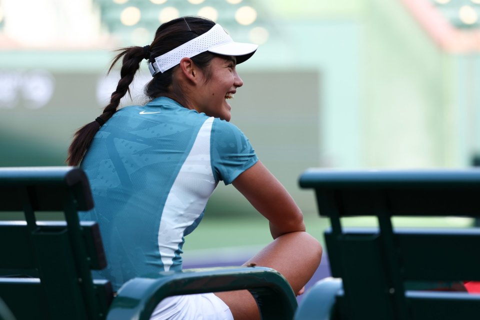 Emma Raducanu smiling while sitting on a bench.