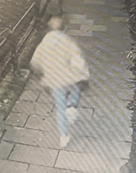 Blurry security camera image of a person walking on a sidewalk.