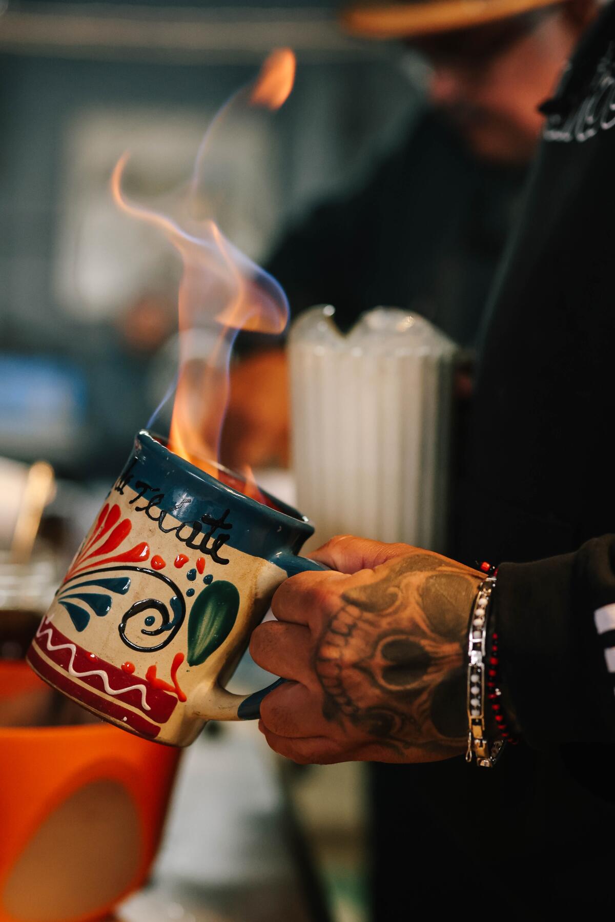 A tattooed hand holding a colorfully decorated mug