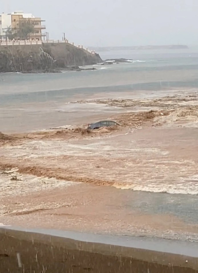 Car submerged in floodwaters on a beach.