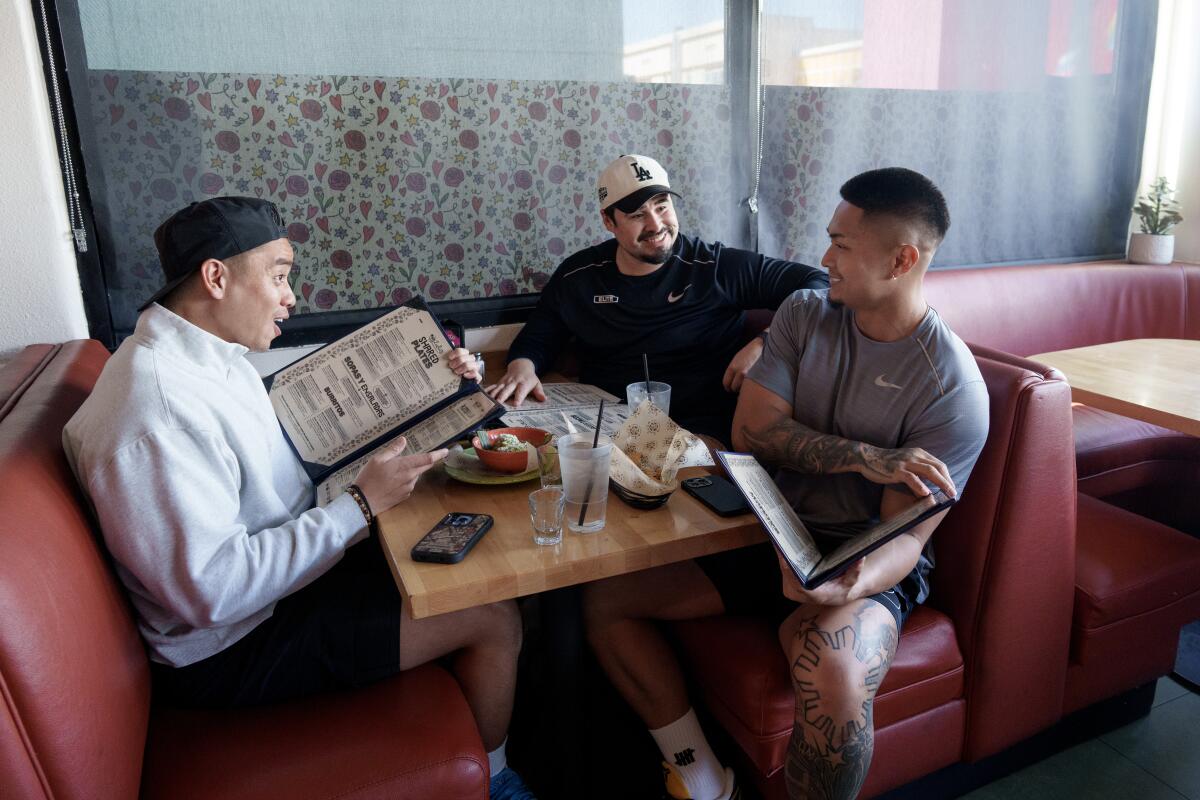 Three people in a restaurant booth talking and looking at menus